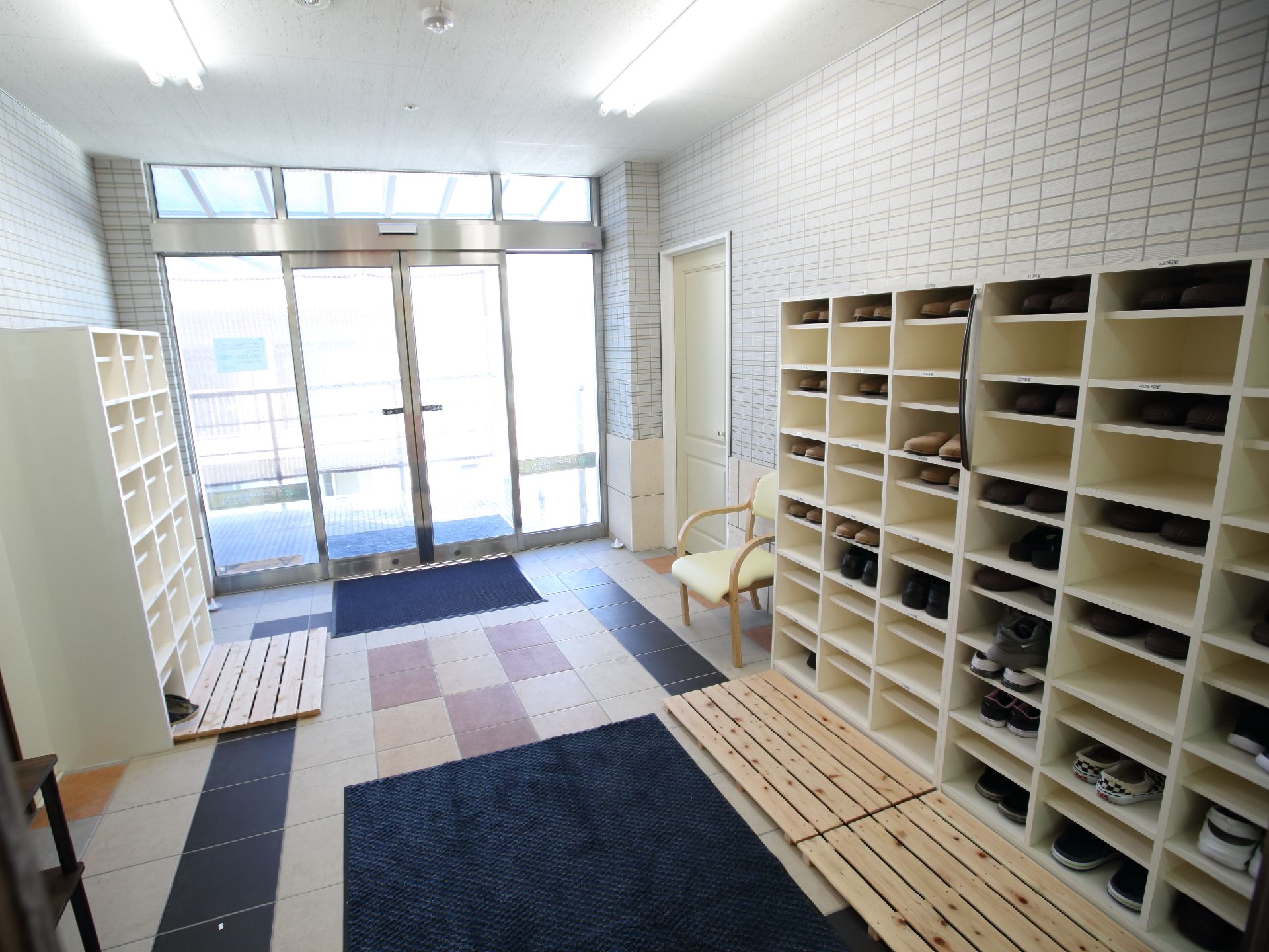 椅子が置かれ、下駄箱の前にすのこが敷かれた、ガラス製の自動扉の玄関