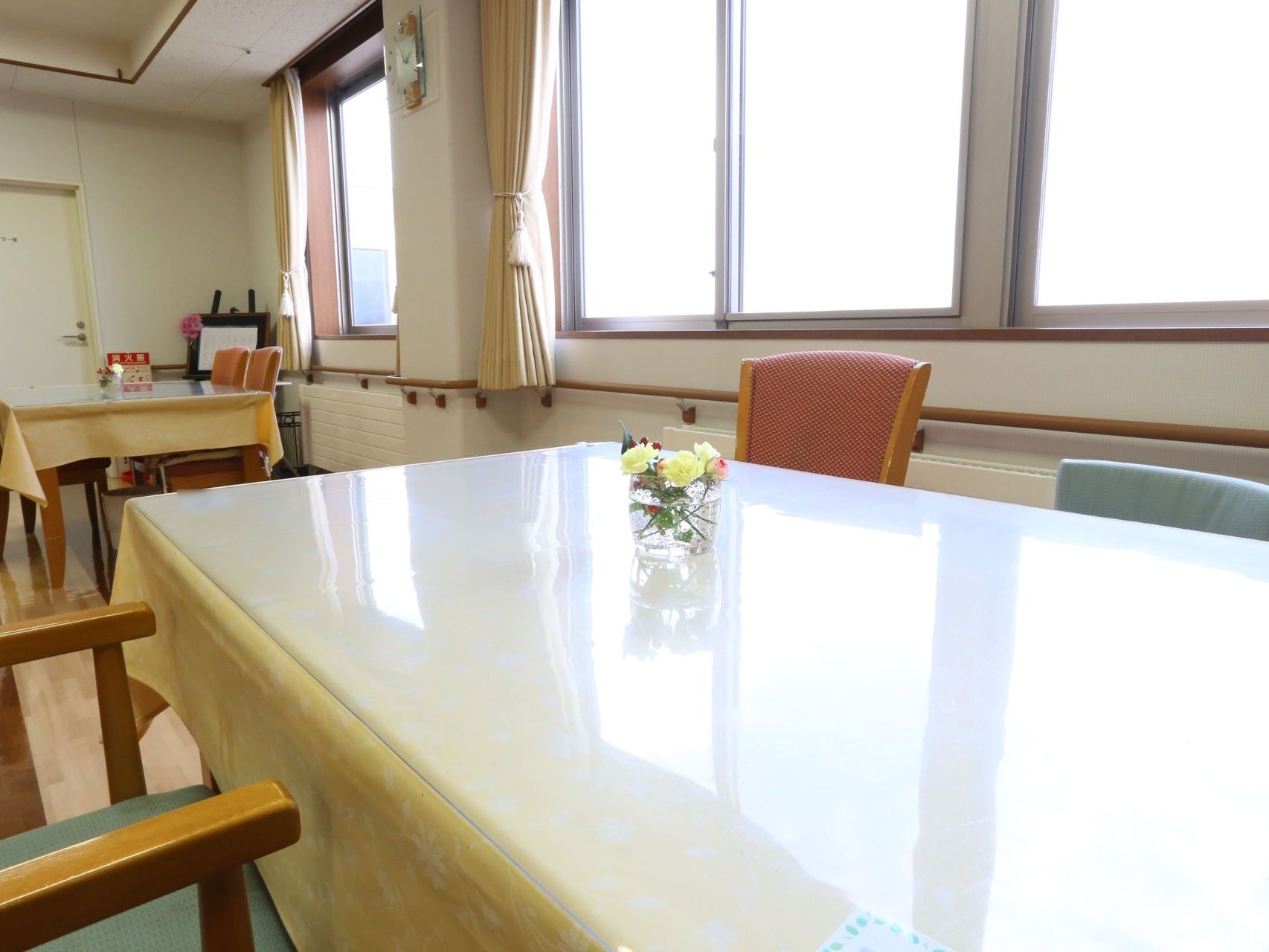 窓から陽射しが入る明るい部屋に、ダイニングテーブルが並べられている。テーブルには黄色いクロスが掛けられている。