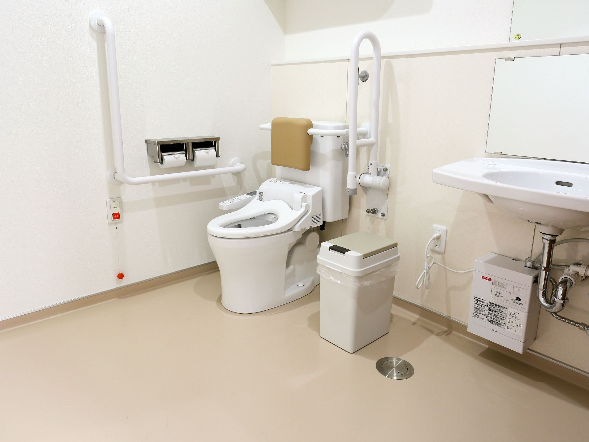 手すりや背もたれが付いた便座と洗面台が付いたトイレ