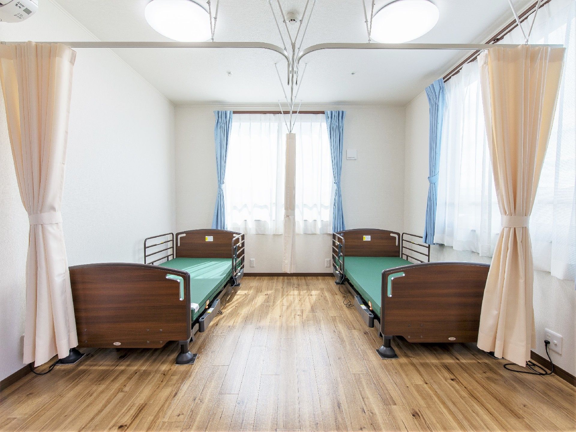介護用ベッドが二つ置かれたフローリングの居室には大き目の窓が複数付き、カーテンで仕切られている。