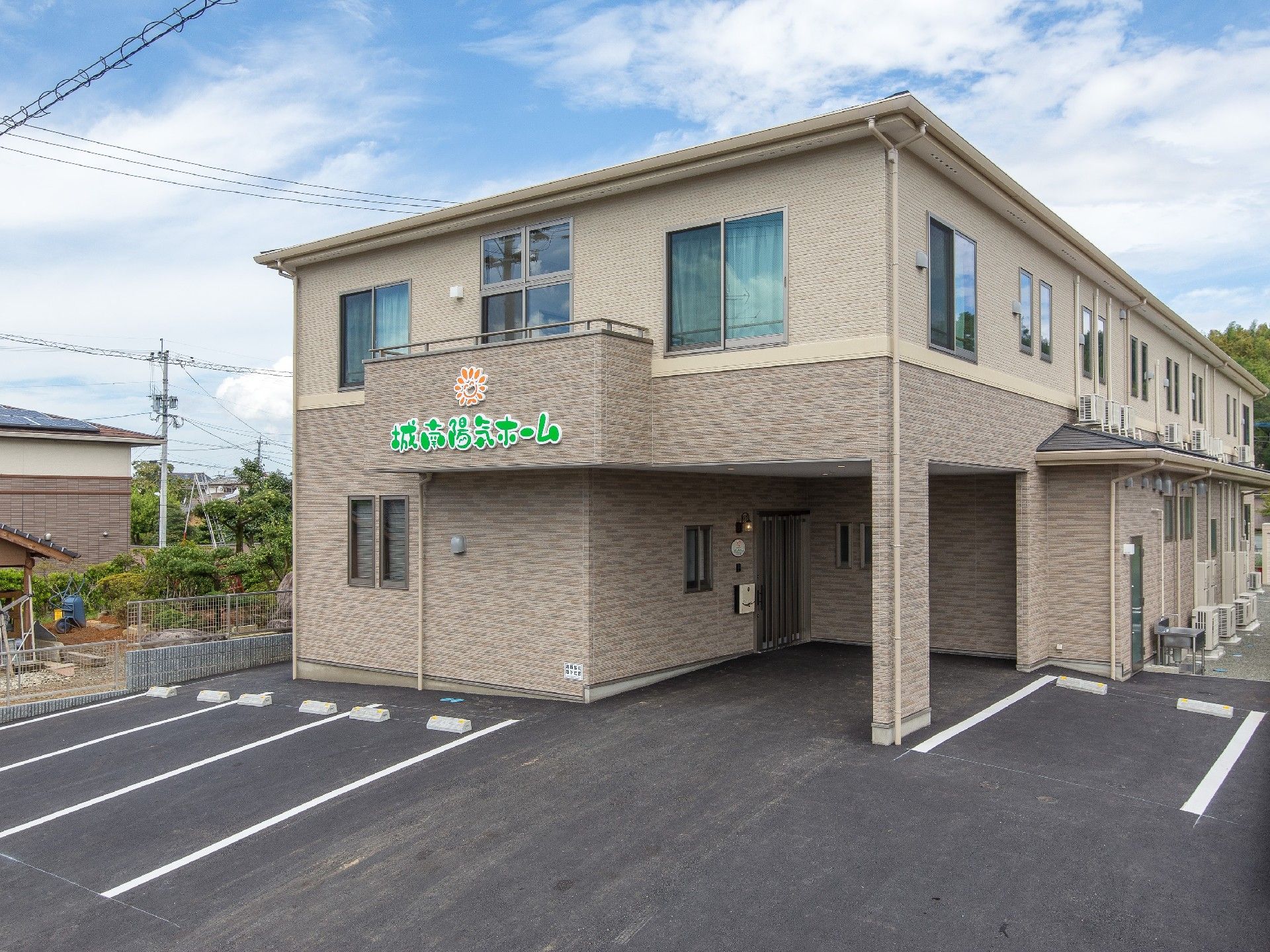 広い駐車場が付いた2階建ての建物はベージュ系。駐車場もついている。