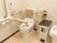固定の手すりと可動式の手すりが取付けられているトイレである。ふた付きのゴミ箱が置かれ、床には掃除道具もある。