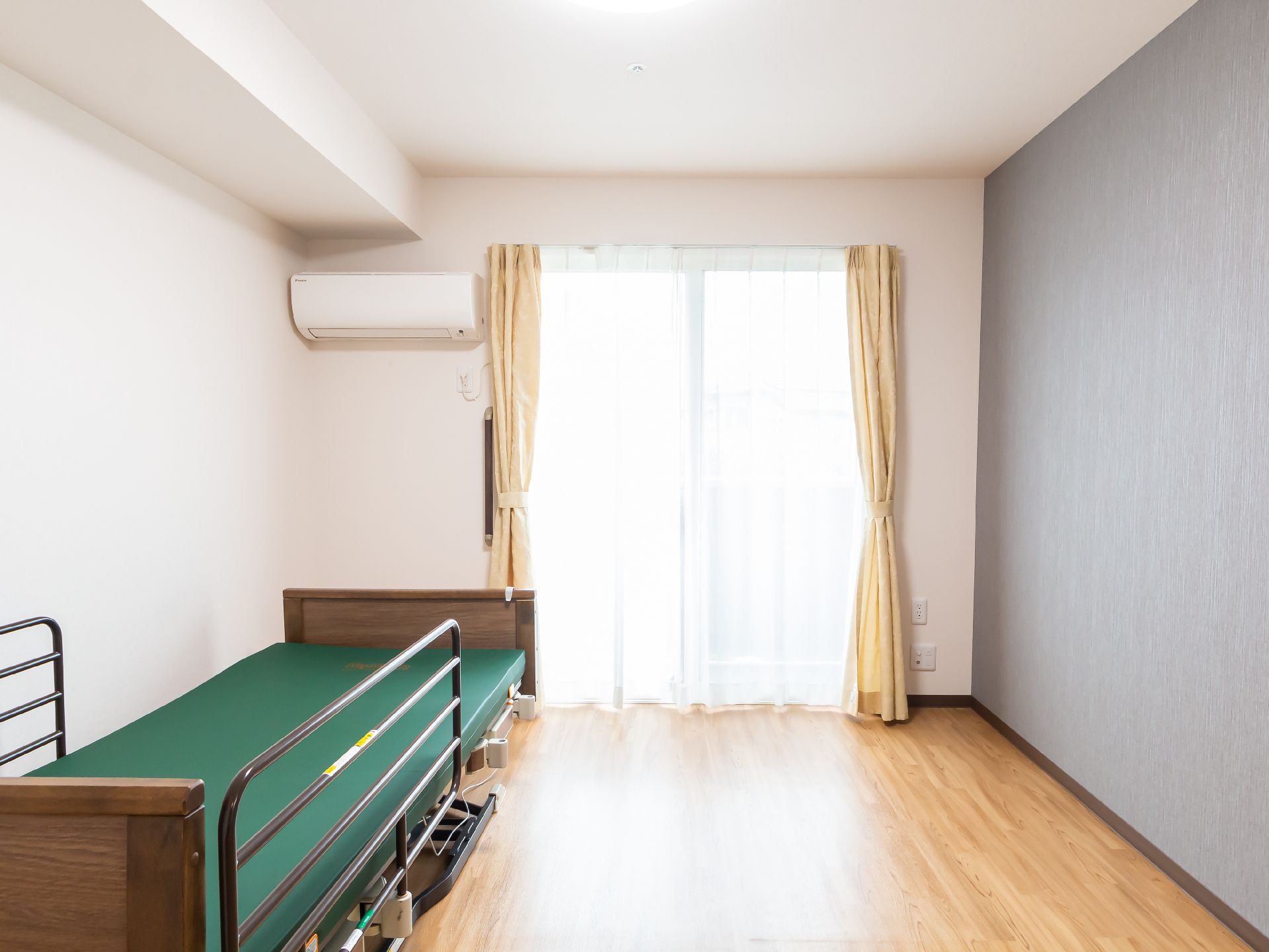 ベッドとエアコンと大きな窓がある白い壁紙の部屋