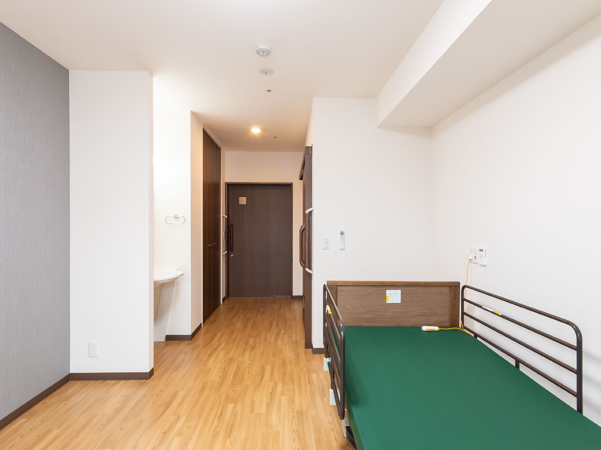 緑のマットレスを敷いたベッドが壁沿いに置かれている白い壁紙の部屋