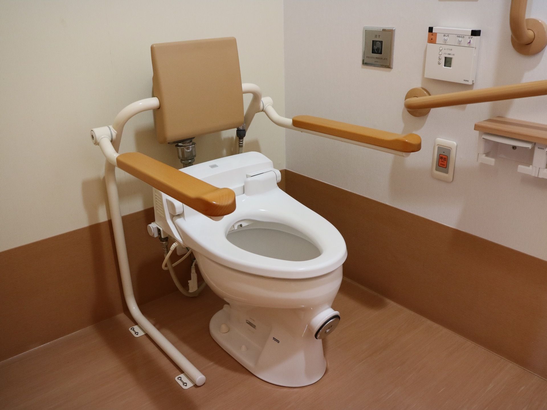 温水洗浄機能付きのトイレで、センサーで水が流れる仕組みになっている。便座には背もたれやひじ掛けが設置されている。