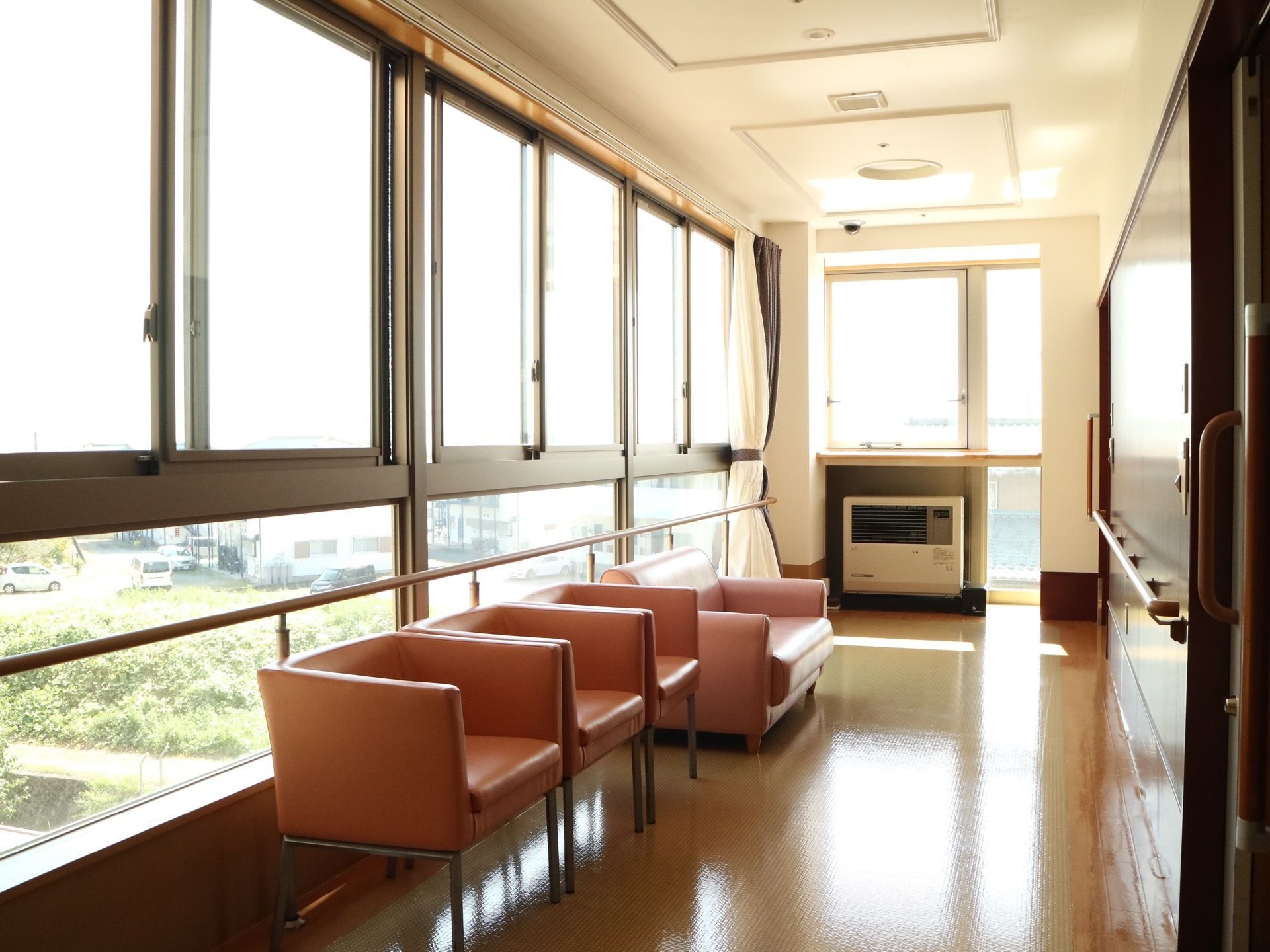 一面に窓が設置されている、開放的な廊下。暖房が完備されており、通路の端には複数のソファーが配置されている。