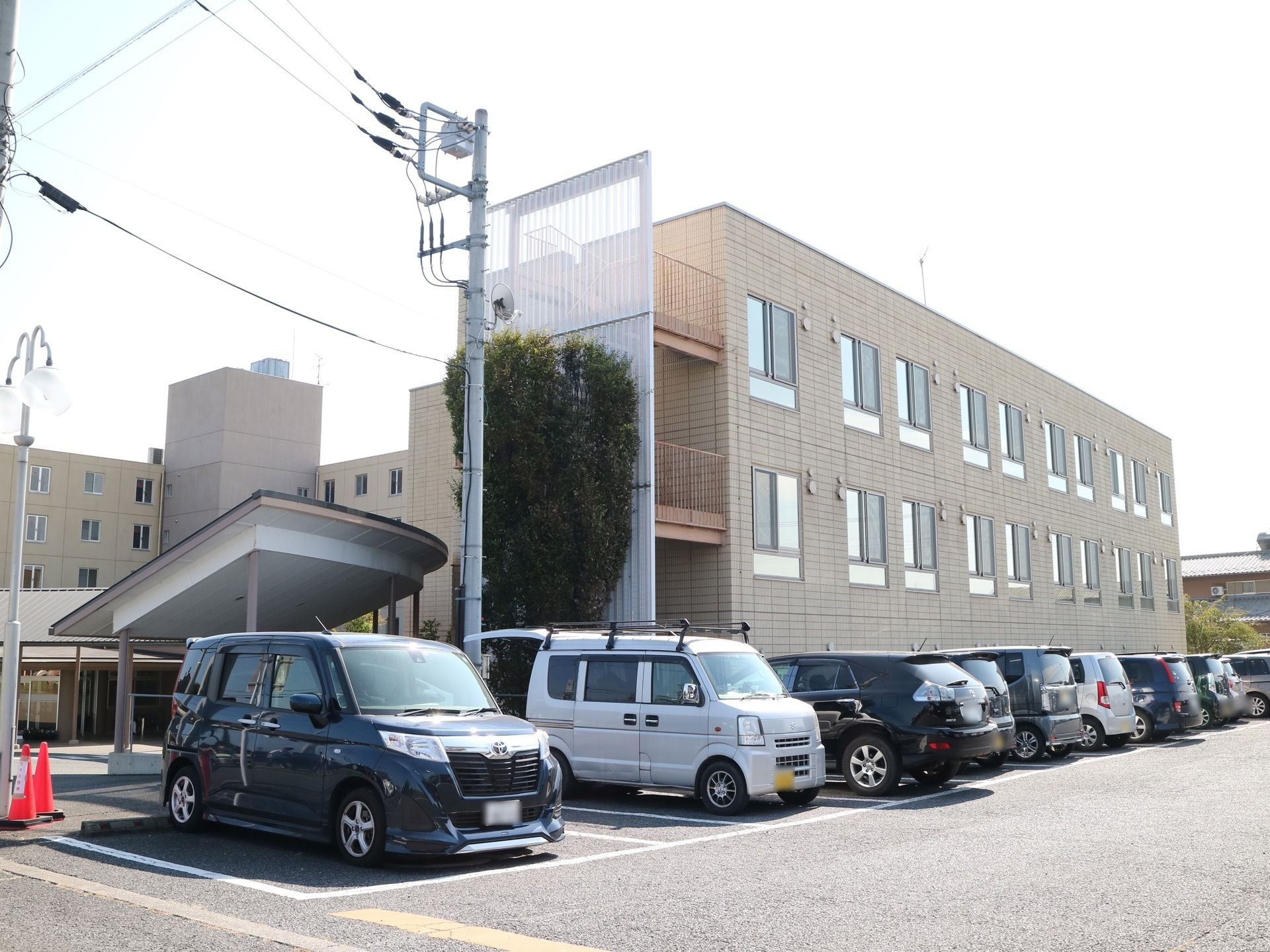 施設敷地内にアスファルトで舗装された広い駐車スペースが設けられており、たくさんの車が停められている。