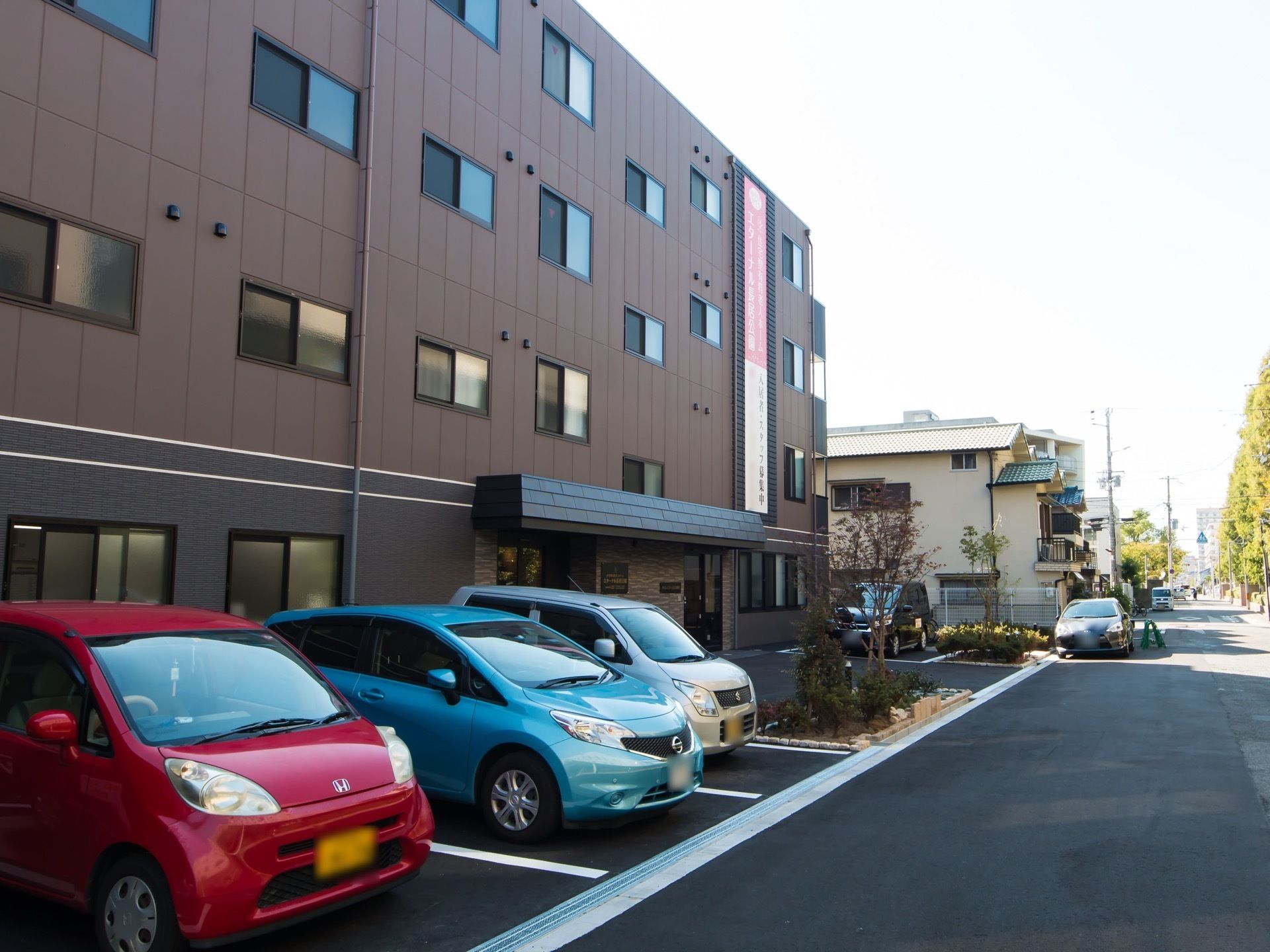 施設敷地内にアスファルトで舗装された駐車場が設けられており、白線が引かれている。数台の車が停車されている。