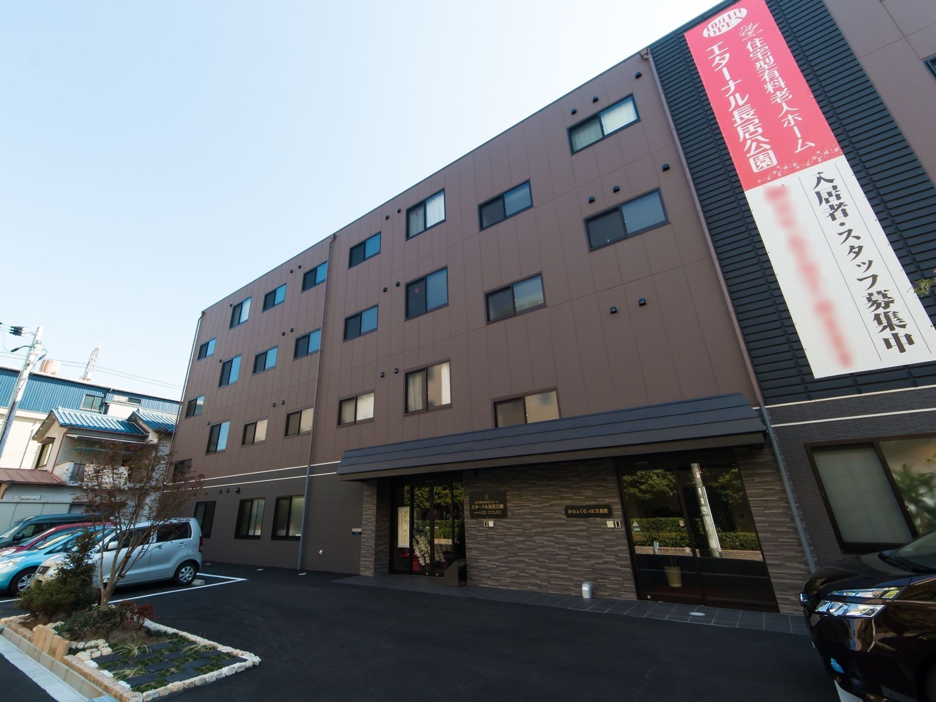 4階建ての建物はブラウンで道路に面していて、駐車スペースもある。