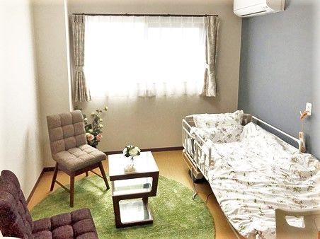 寝具がセットされたベッドやテーブルセットが置かれた居室。季節の花も飾られている。