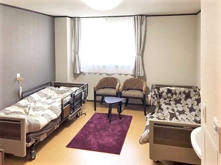 紫色のカーペットが中央に置かれ、両サイドにベッド、窓際には椅子が置かれている。