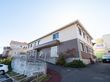 施設は高台に建てられた１階と２階で色の異なる２階建ての建物である。玄関前は駐車スペースがあり、車が１台停められている。
