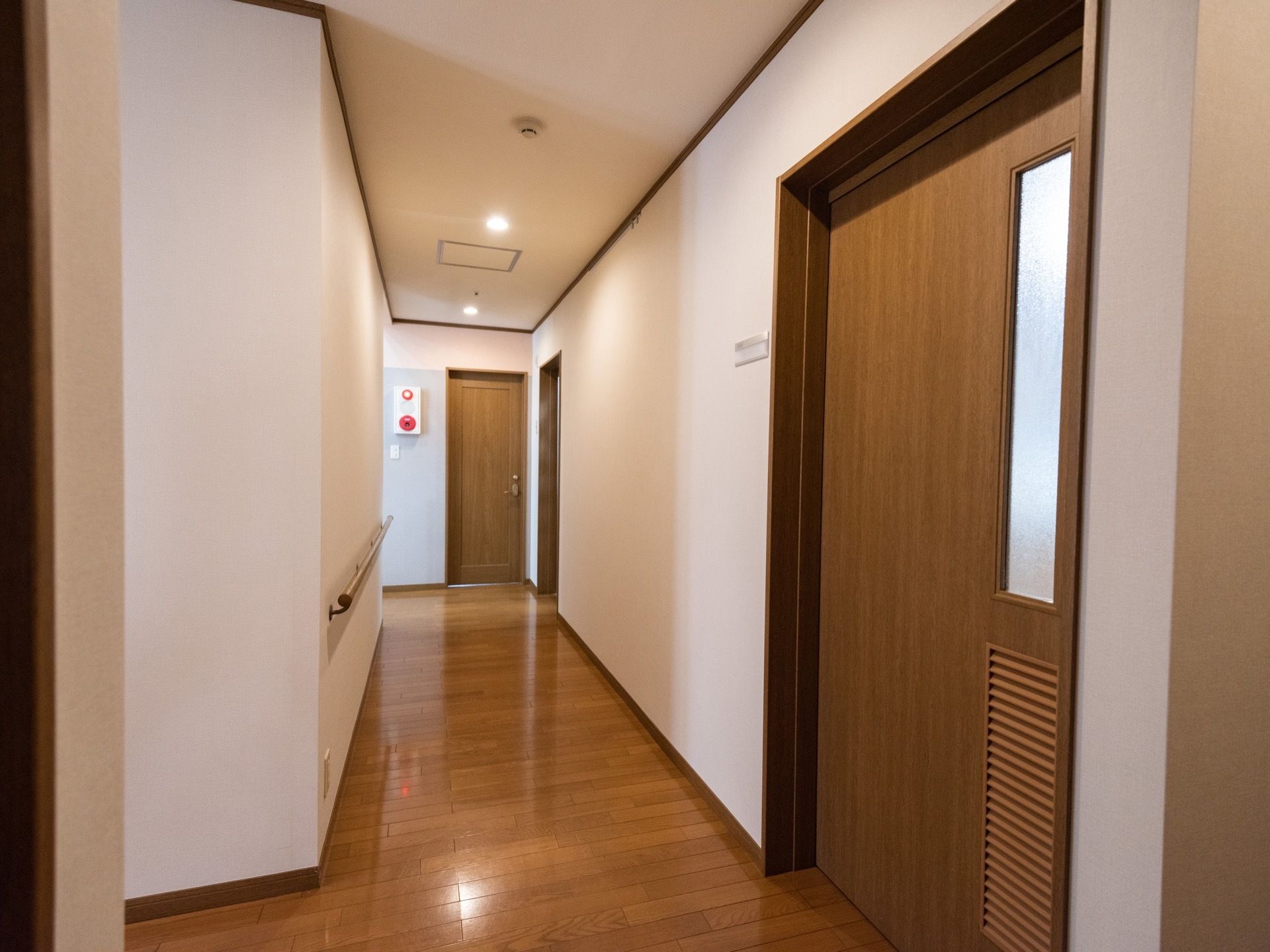 通路には火災報知システムが設置してある。壁に沿って個室のドアが並んでおり、建具はフローリングとおなじ木調である。