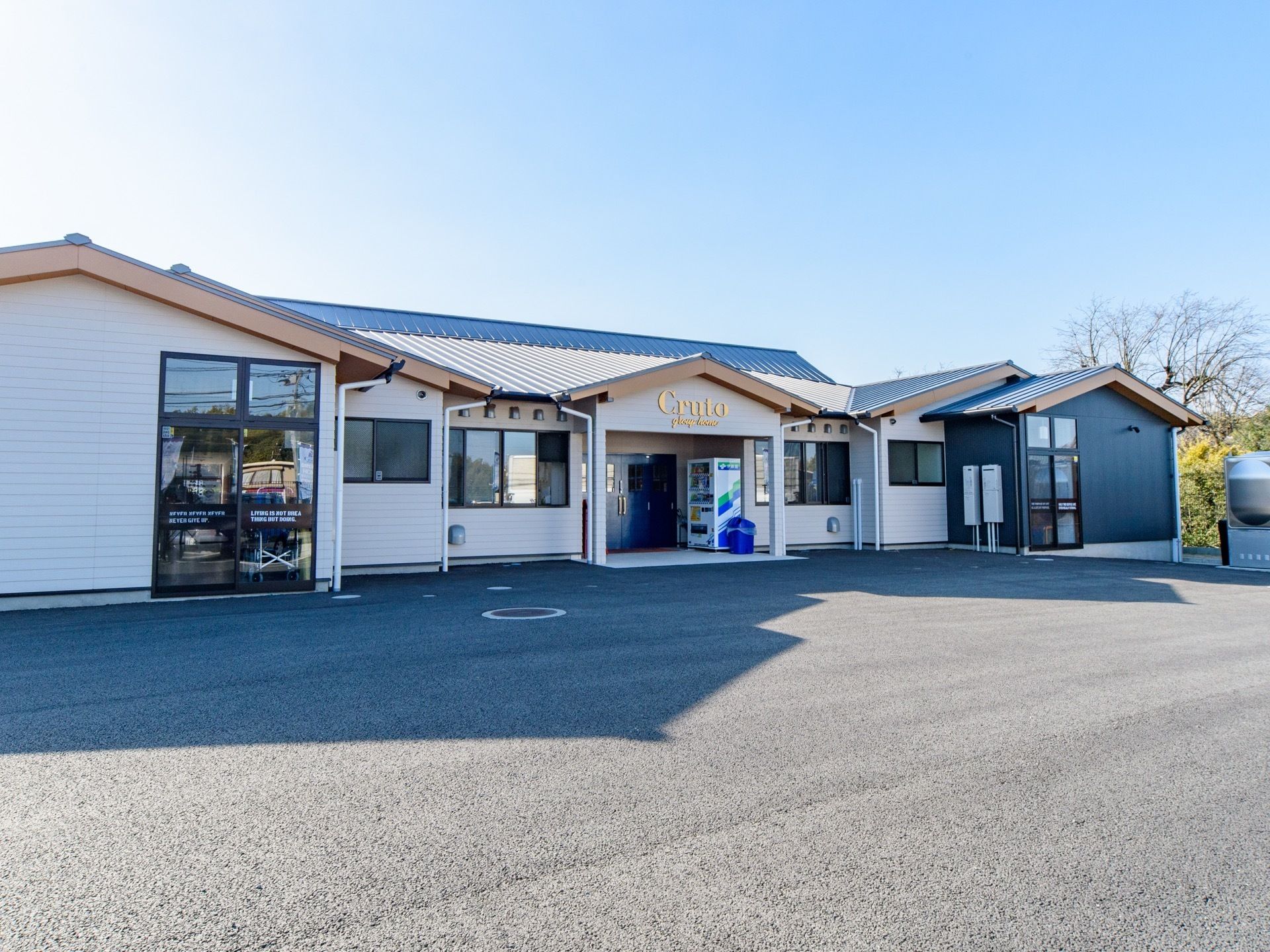 １階平屋建ての建物で、施設前の路面はアスファルトで舗装されている。自動販売機の横にゴミ箱が置かれている。
