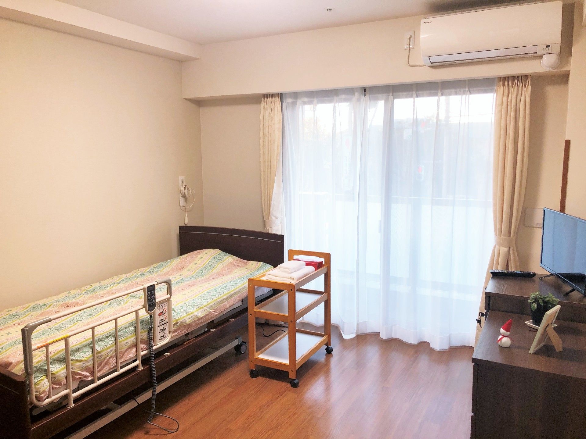 フローリング貼りの部屋に、ベッドとエアコンとチェストが置かれている