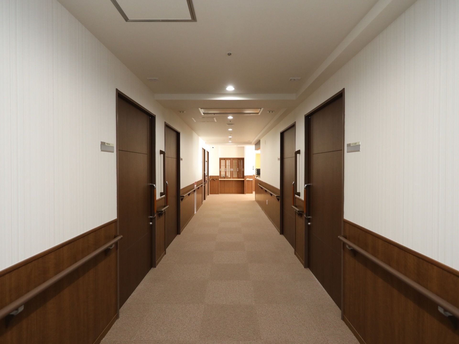 フロアクッションが敷き詰められた廊下で、白い壁でこげ茶色のドアが付いている。ドアの横には、大きな手すりが付けられている