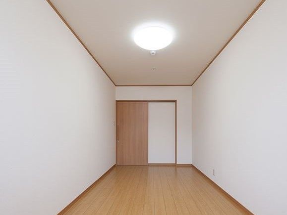 シンプルなフローリングの居室。家具などはなく、照明と出入り口の引き戸があるのみ。