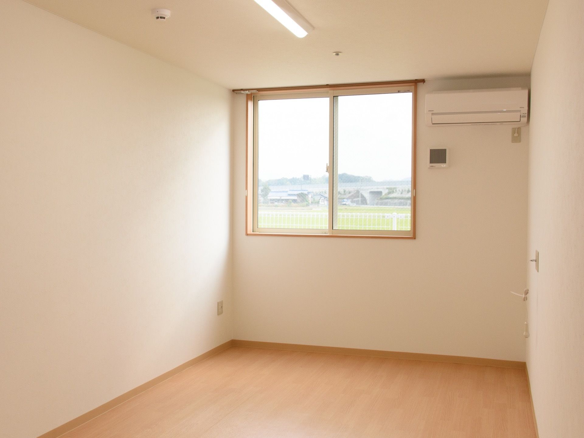 居室の突き当たりに窓があり、その横にはエアコンを設置。窓からは緑が広がるのどかな風景が見える。