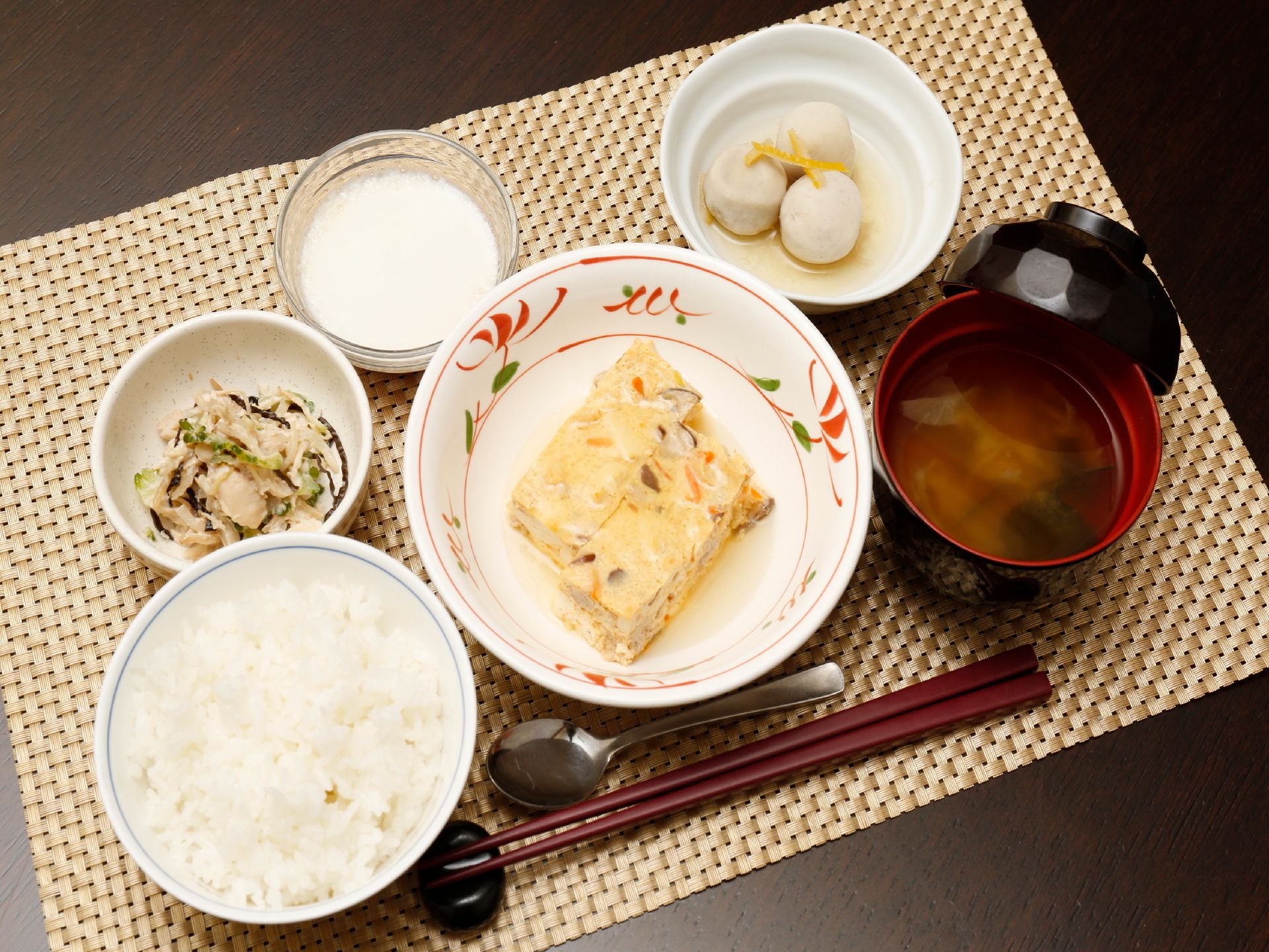純和風の食事がランチョンマットの上に置かれている。主菜に里芋などの副菜が2品、ごはんに味噌汁が用意されている。