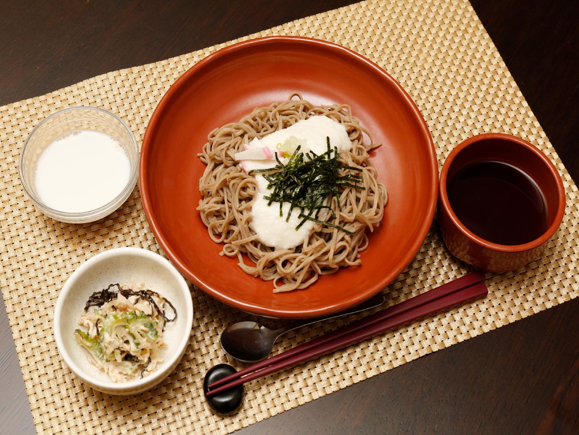 赤茶色の漆器の上にとろろそばが用意されている。副菜とデザートもついており栄養バランスにも配慮されている。