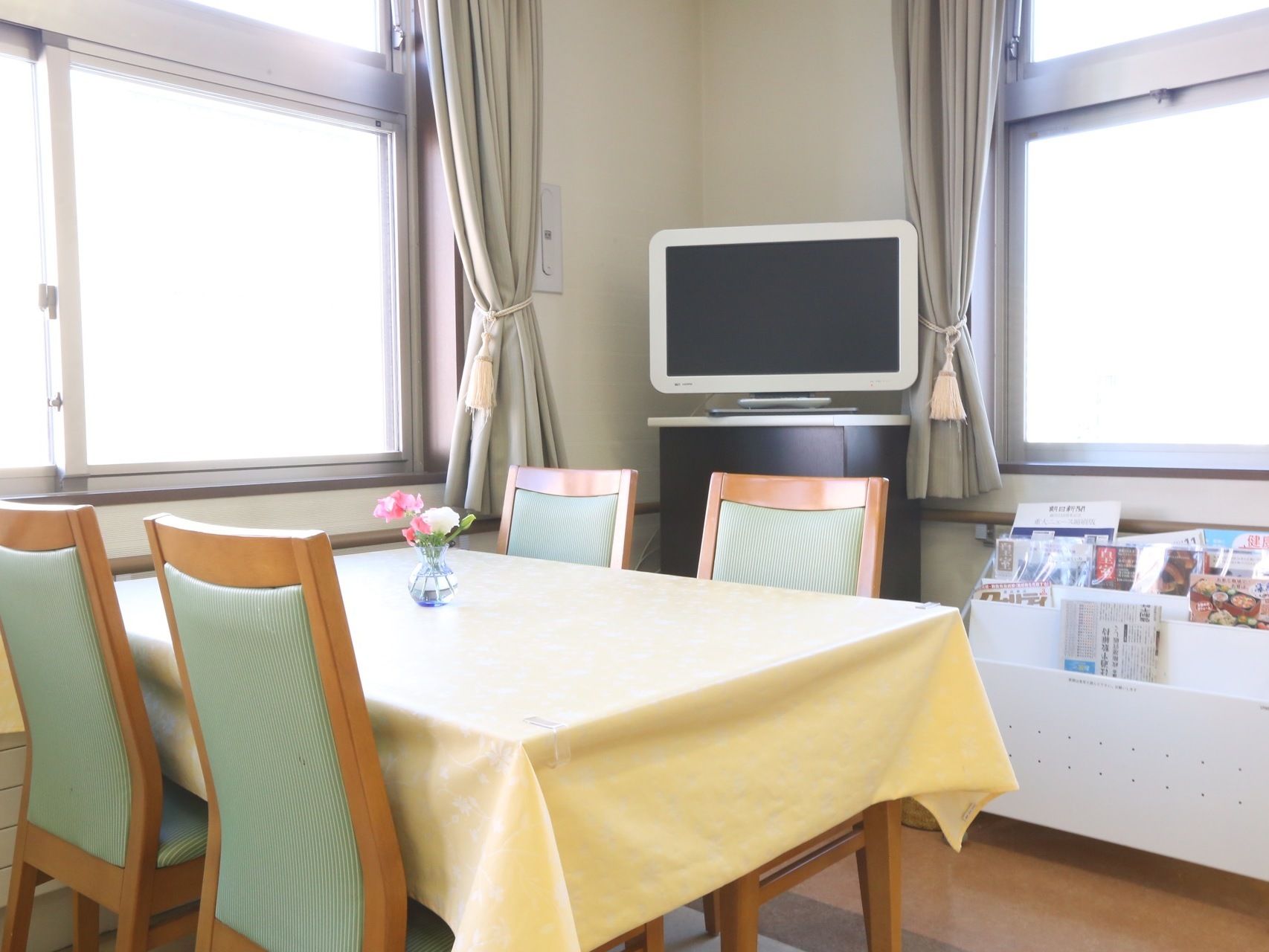 白が基調の日当たりのよい明るい食堂である。テーブルクロスが掛けられており、カーネーションが生けられている。