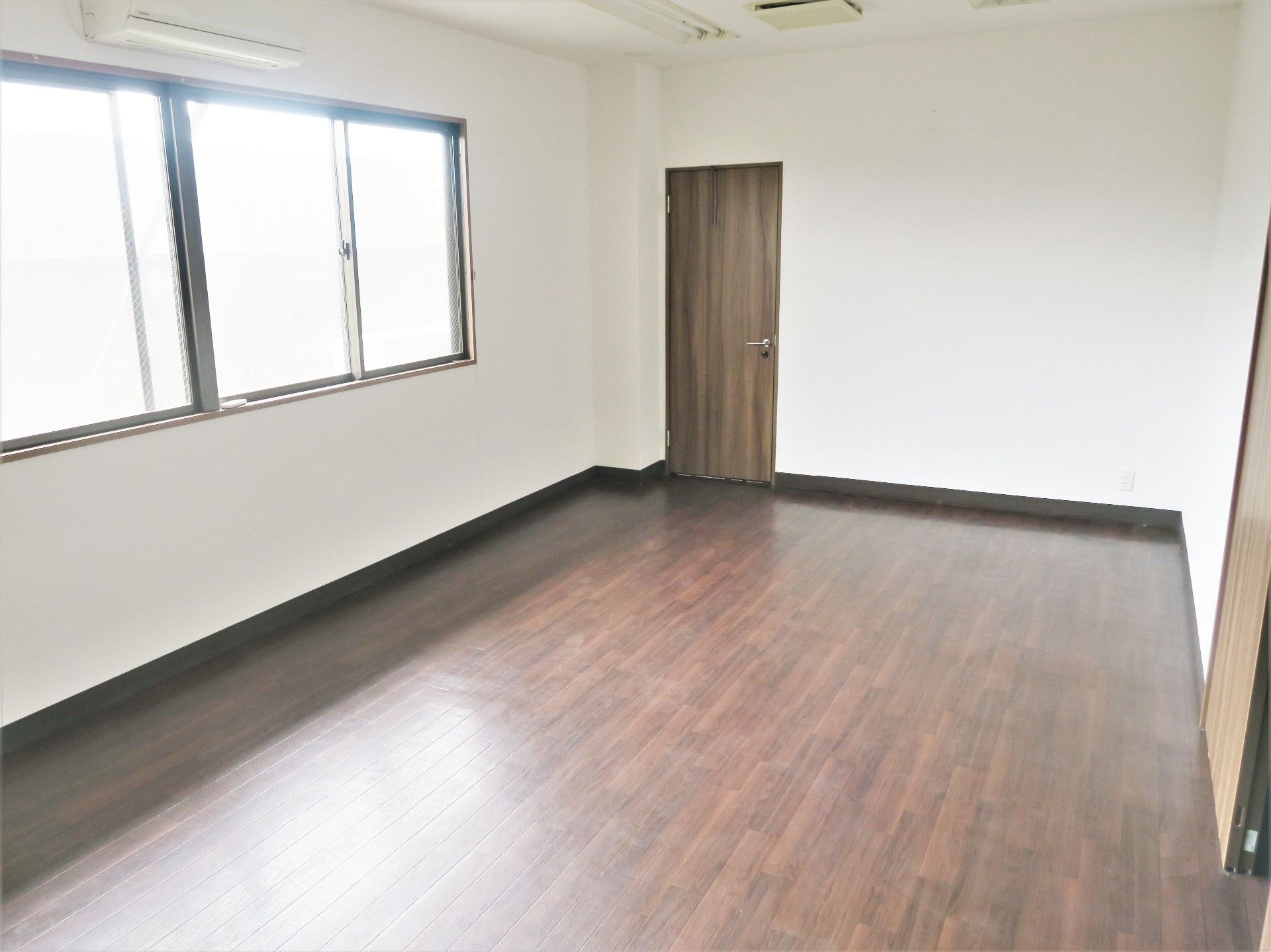 大きな窓が付いたフローリングの居室に家具はなく、エアコンが付いている。