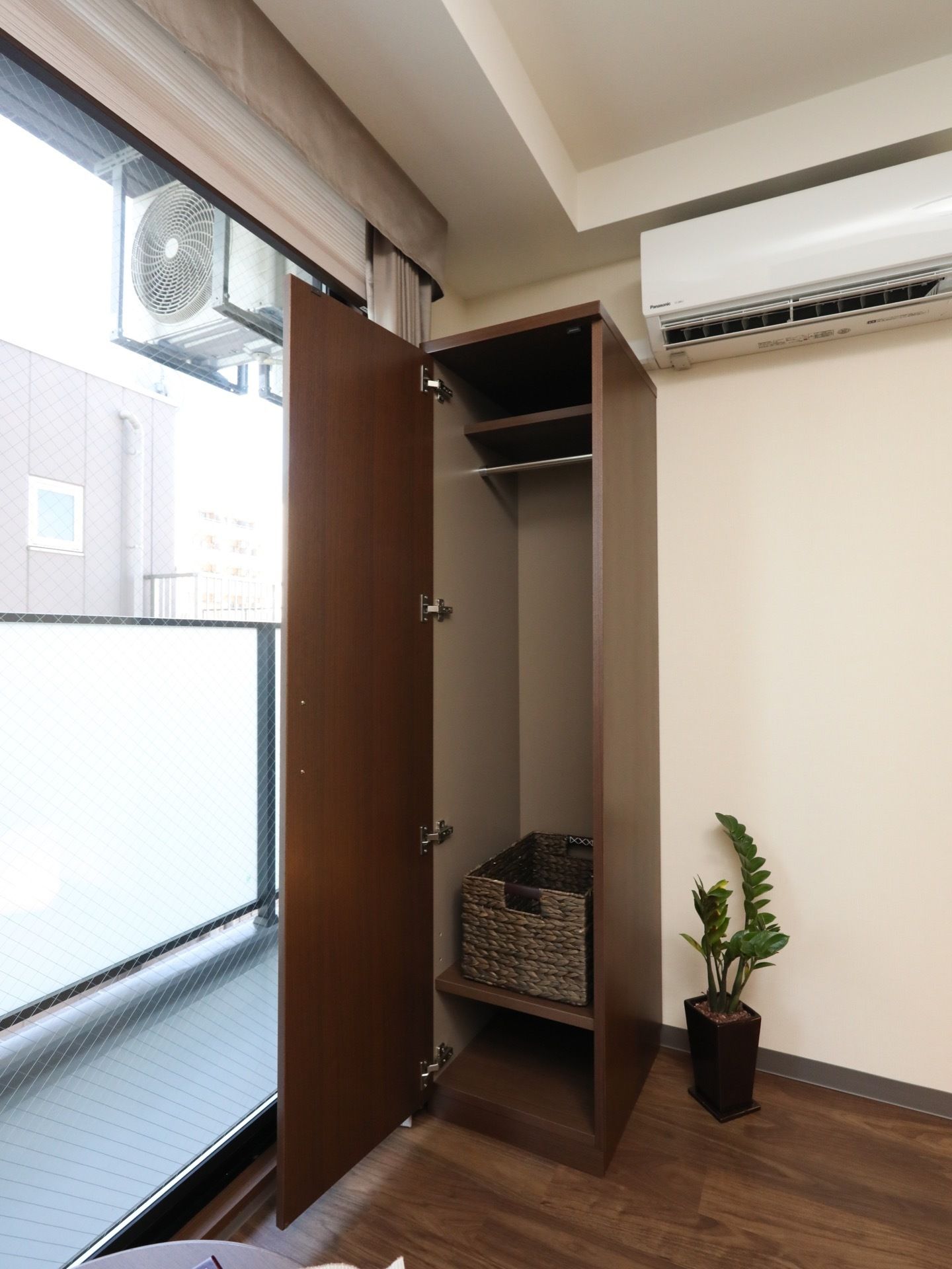 窓際に、ダークブラウンのクローゼットが備わっている。中に棚板とハンガーポールがあり、小さなカゴも入っている。