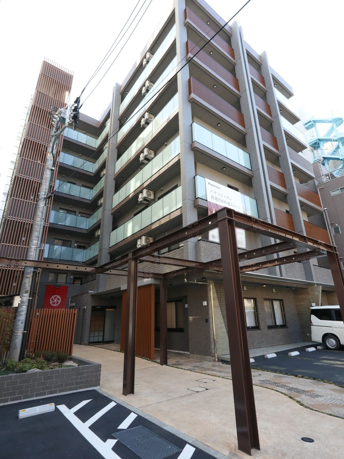 7階建てのマンションのような外観の建物で、敷地内は舗装されており、駐車スペースが複数備わっている。建物の左側には、非常階段がある。