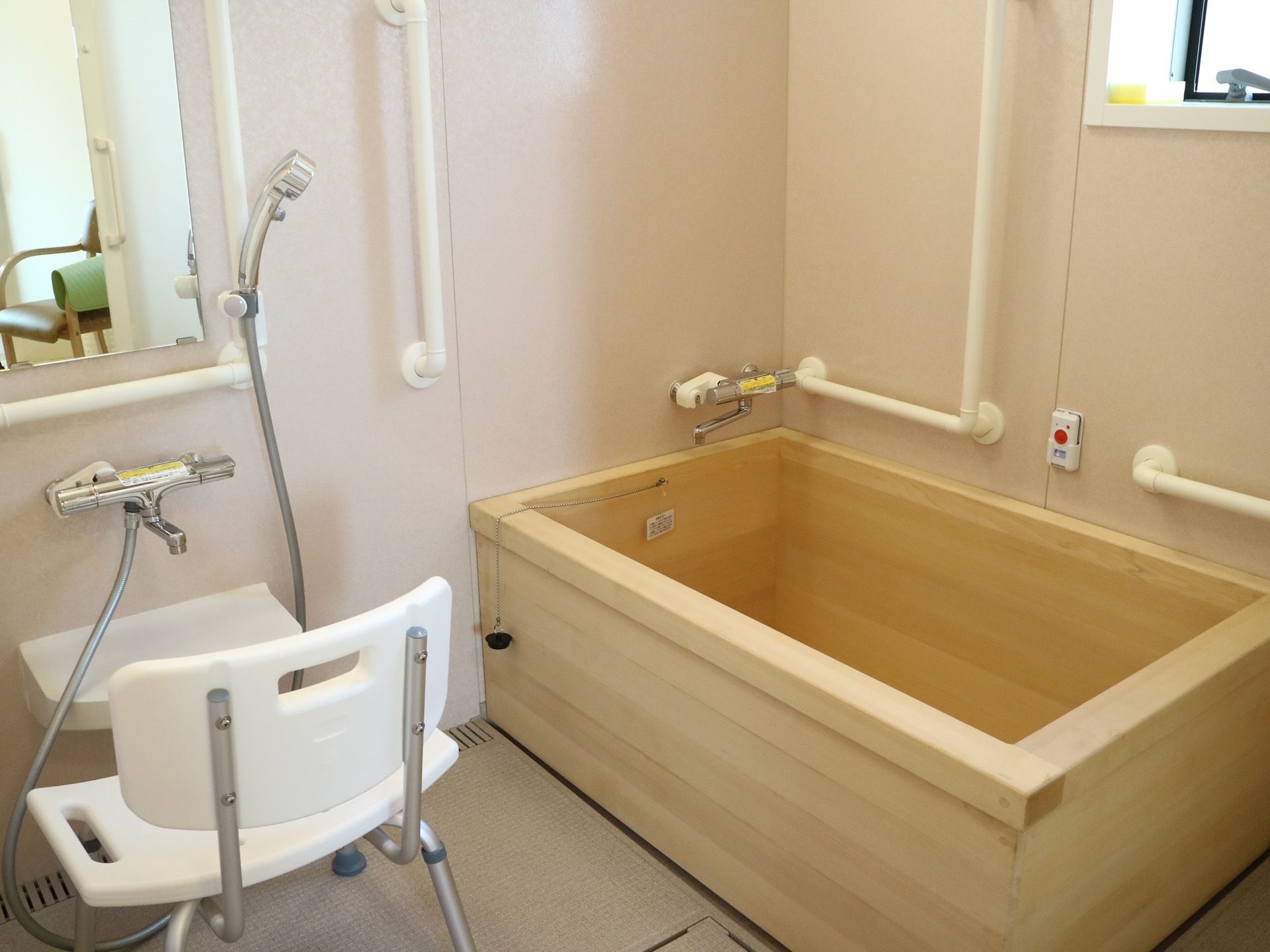 木製の浴槽で、壁には手すりが２つ設置されている。その間には、スイッチのついた機器がついている。洗い場にはシャワーチェアがある。