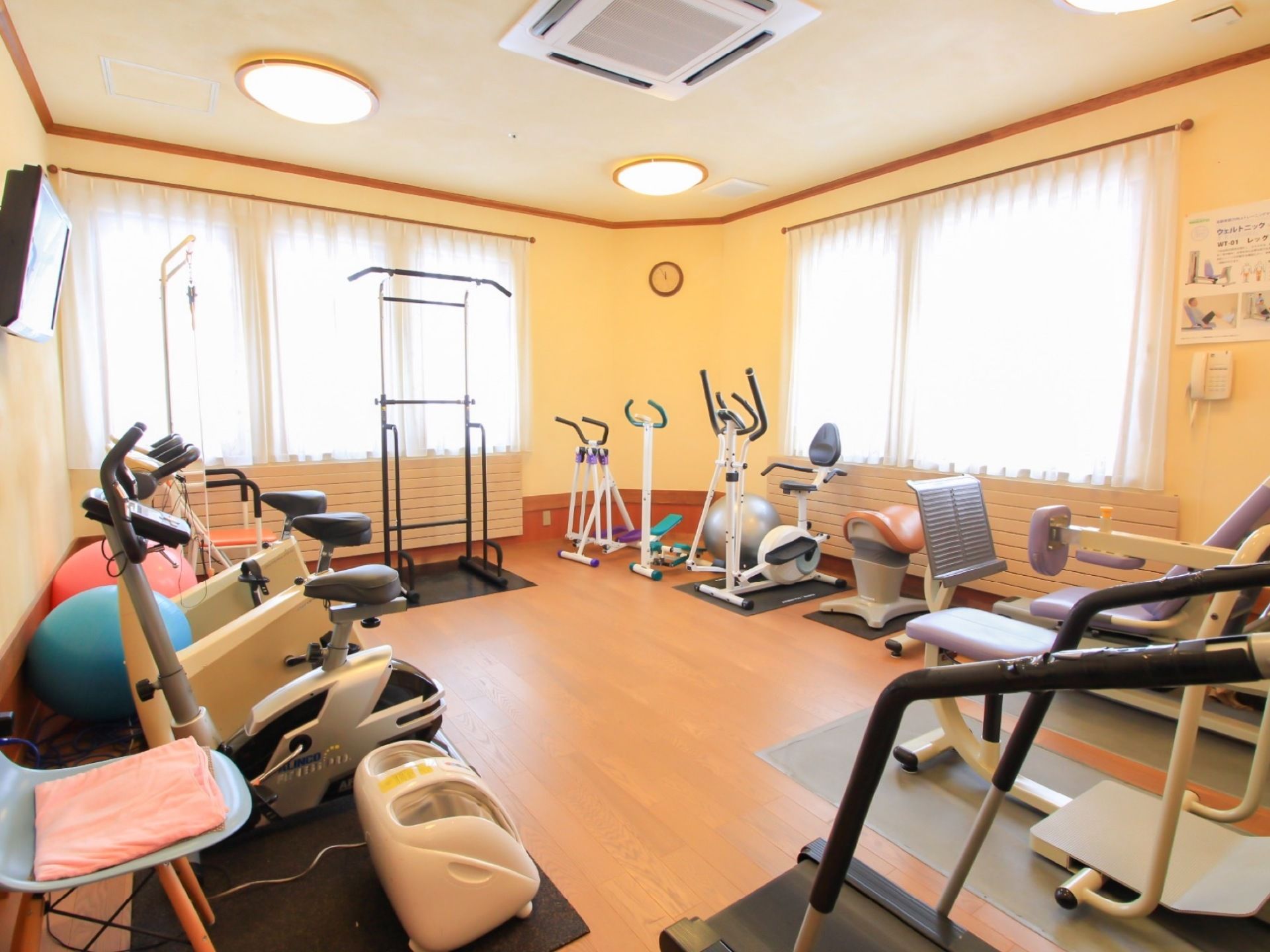 レースカーテンが掛けられた窓から光が入る広々とした部屋である。部屋の壁に沿ってたくさんの健康器具が置いてある。