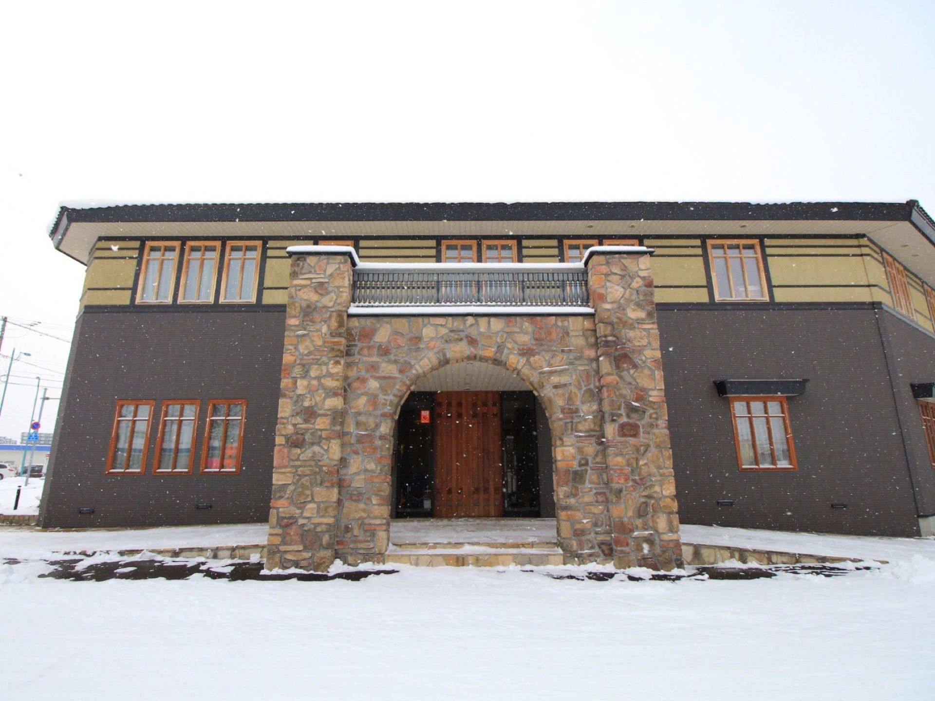 木枠がはめられた窓がたくさんある２階建ての建物がある。地面には雪が降り積もり、空はどんよりと曇っている。