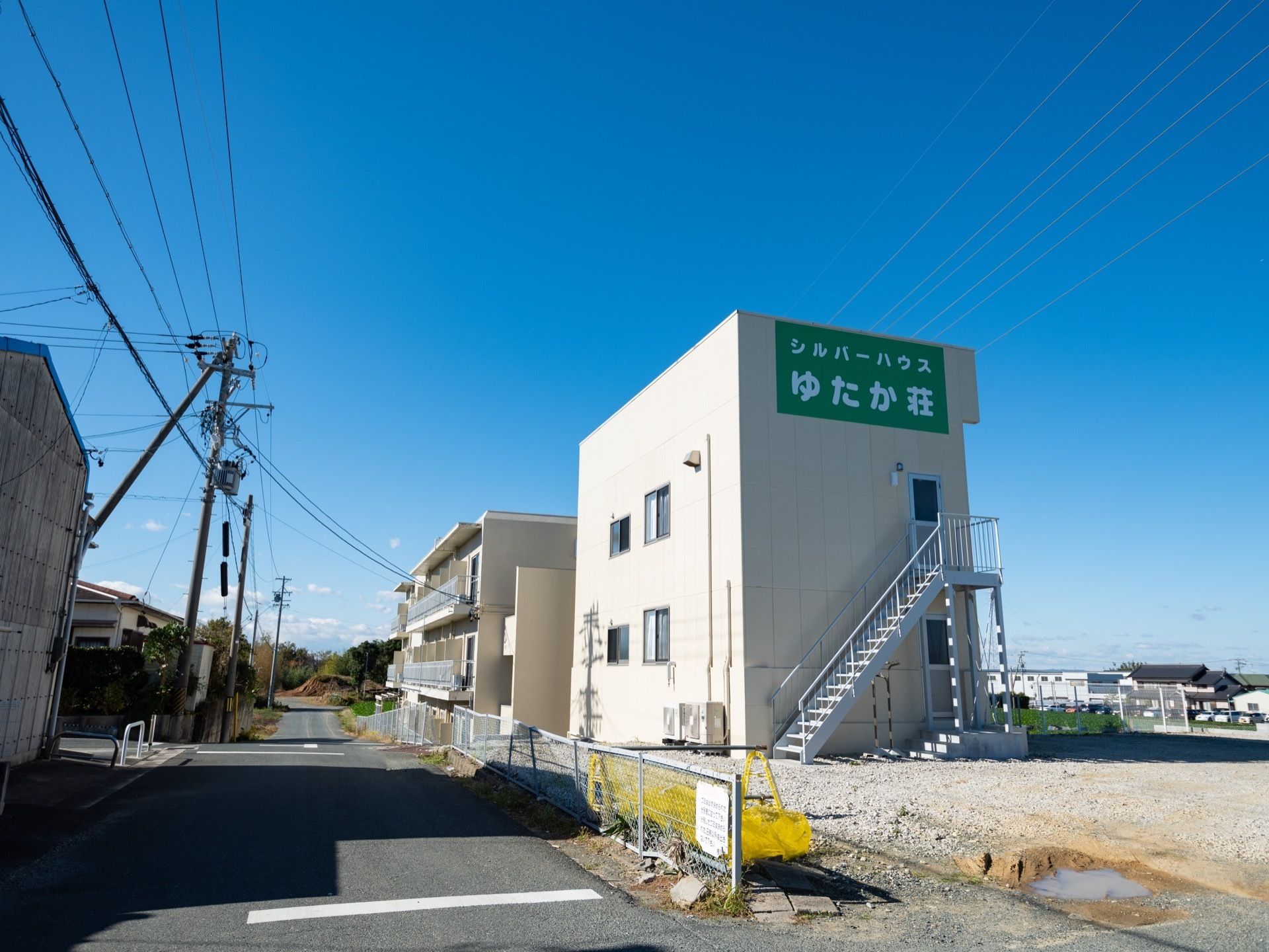 大きな緑の看板が外壁に取り付けられ、そこには白い文字で施設名が表示されている。すぐ下には外階段と出入り口が設置されている。
