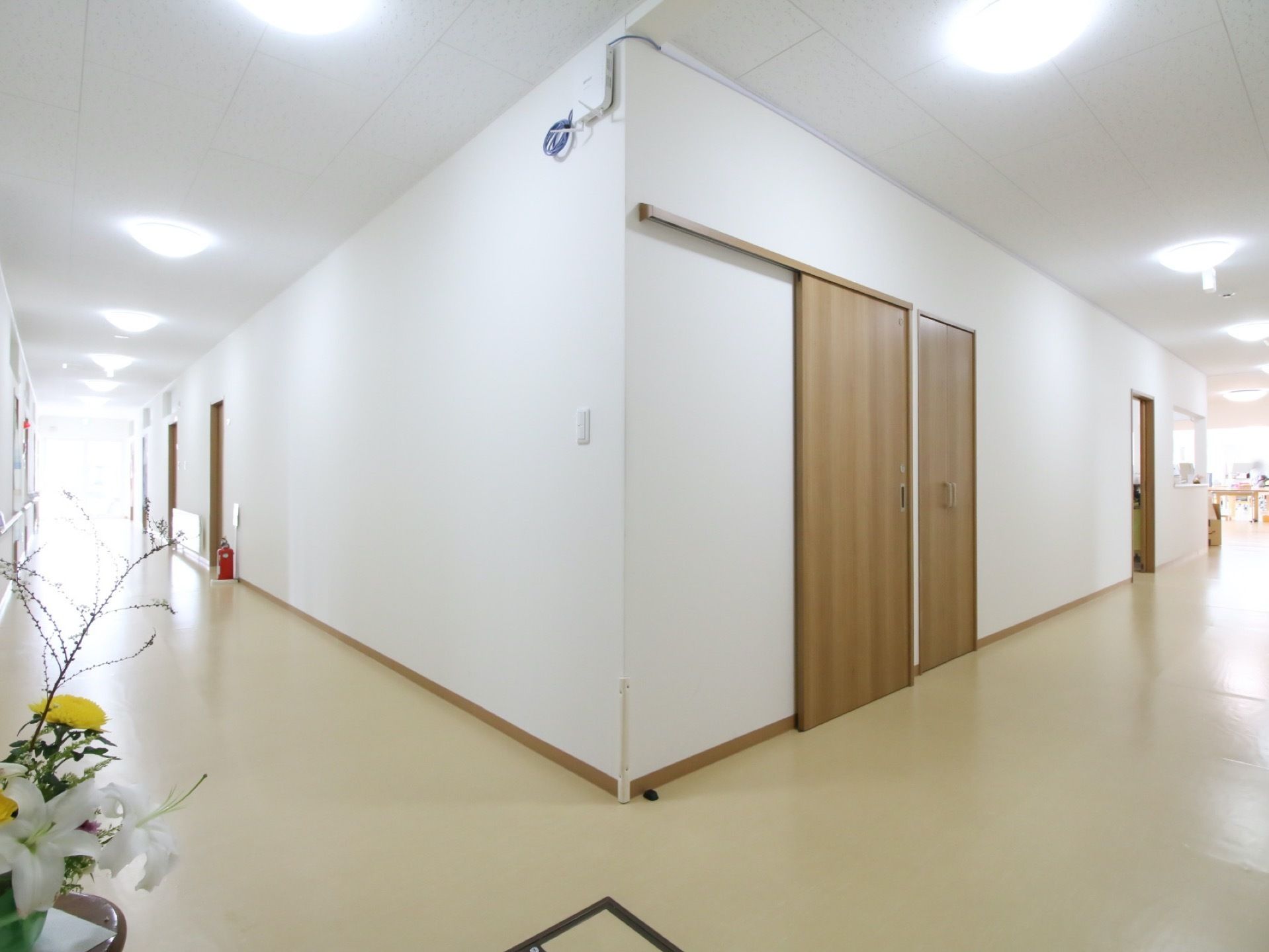 建物内の廊下は、床と壁、そして天井が全体的に白いカラーリングとなっている。左手奥には消火器が置いてある。