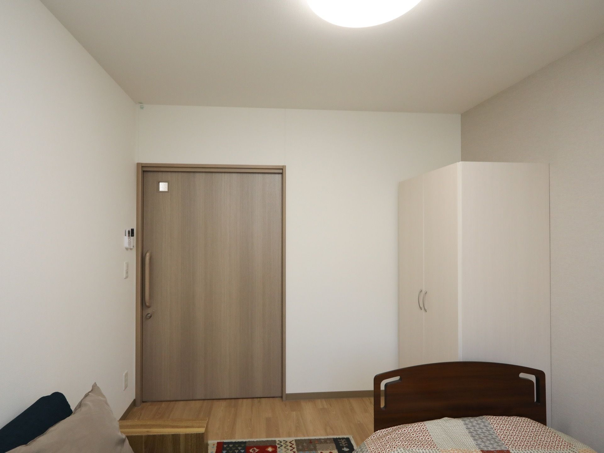 真っ白な壁が美しい居室である。LEDライトや介護用ベッド、白い洋服ダンス、クッション付きのソファが完備されている。