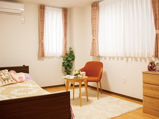 寝具付きのベッドやエアコン、テーブルセットやタンスが置かれた居室には大小の窓があり、それぞれにカーテンとレースカーテンが付いている。