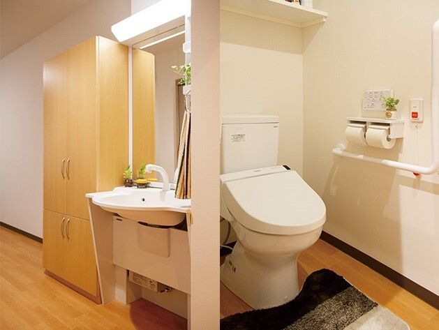 赤い呼び出しボタンが付いたトイレが右側に、左側には車いす対応のデザインの洗面所がある。トイレにはマットが敷かれ、洗面所にはタオルも付いている。