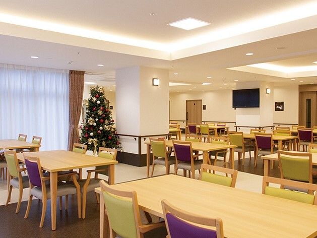 大きなクリスマスツリーが飾られた食堂にはダイニングテーブルが複数並び、壁には手すりが付き、大きな壁掛けテレビも設置されている。