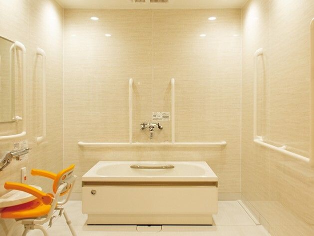 白い手すりがたくさんつけられた一人用の浴室。左側にはシャワーチェアが置かれたシャワースペースがあり、浴槽は３方向から介助が可能。