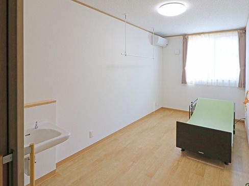 洗面所やエアコンが付いたフローリングの部屋には介護ベッドが置かれ、大きな窓がある。