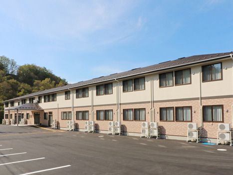 緑が多く近くにある２階建ての建物は日当たりのいい場所に建っていて、大きな駐車場がある。