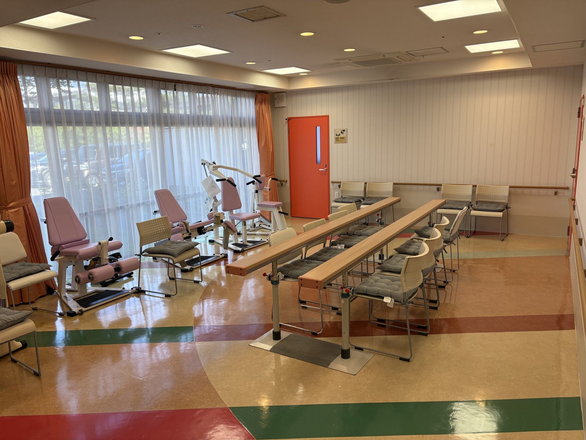 室内の床はカラフルな配色になっており、平行棒のほか、さまざまなトレーニング機器が設置されている。壁には手すりが設けられている。