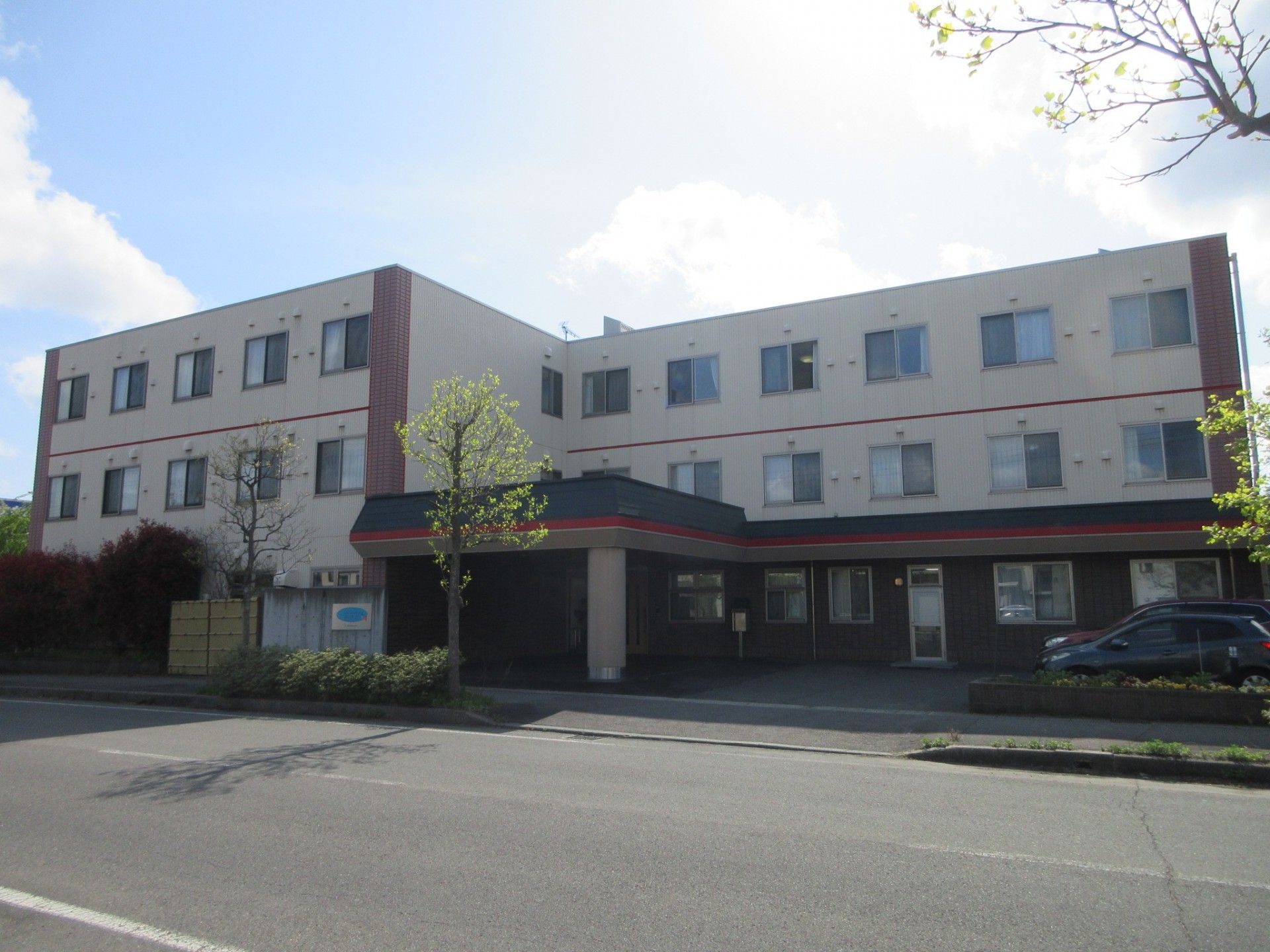 道路に面した敷地に建つ３階建てで、張り出し屋根が付いた広いエントランスがある施設の外観