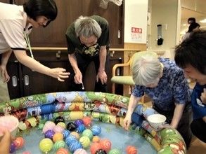 ビニールプールでヨーヨー釣りを楽しむ入居者。スタッフが声をかけている。