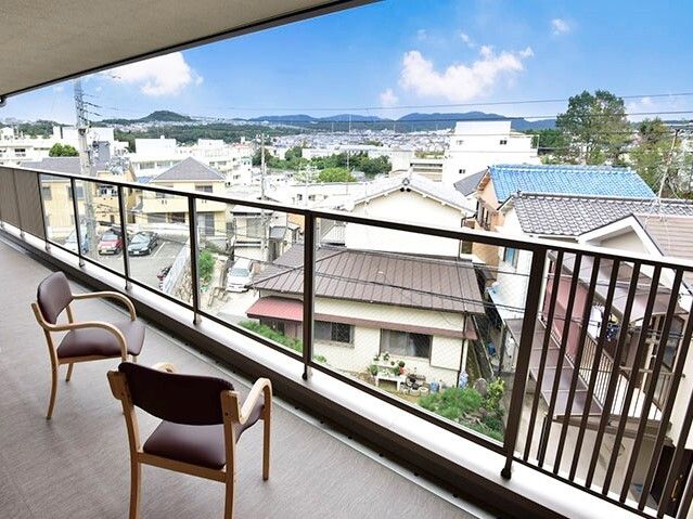 たくさんの住宅が周辺にあり、アットホームな雰囲気。テラスは広く手すりが付き、椅子が2脚置かれている。