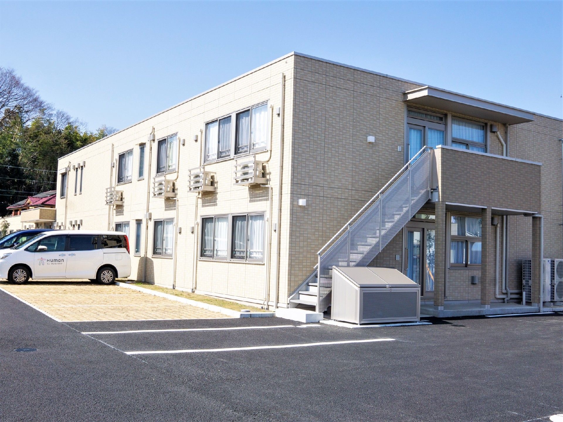 駐車場が付いたベージュの建物。玄関には屋根が付き、庭もある。