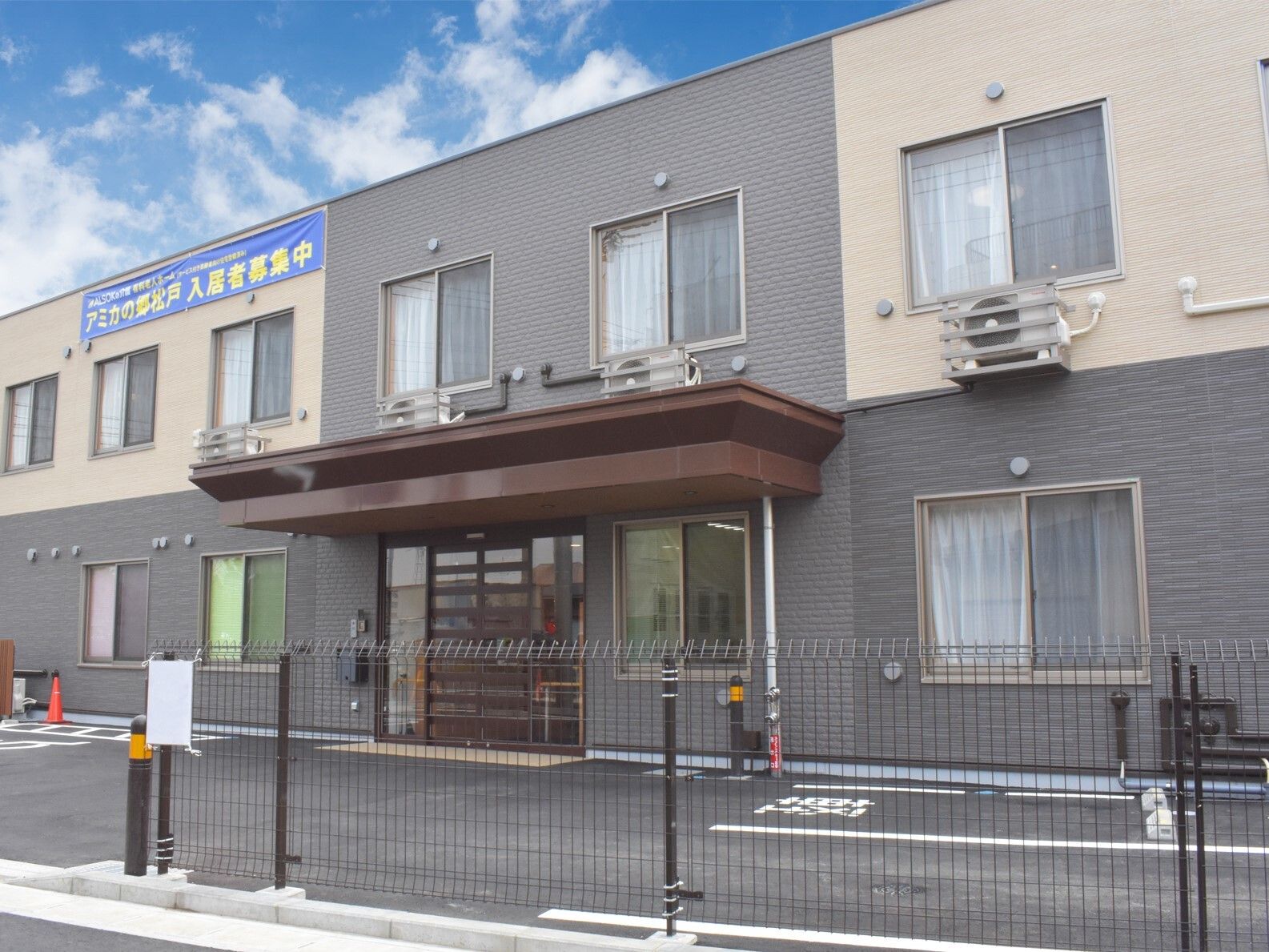 2階建ての建物の玄関には屋根が付き、ベージュとブラウンの2色づかいで落ち着いた雰囲気。