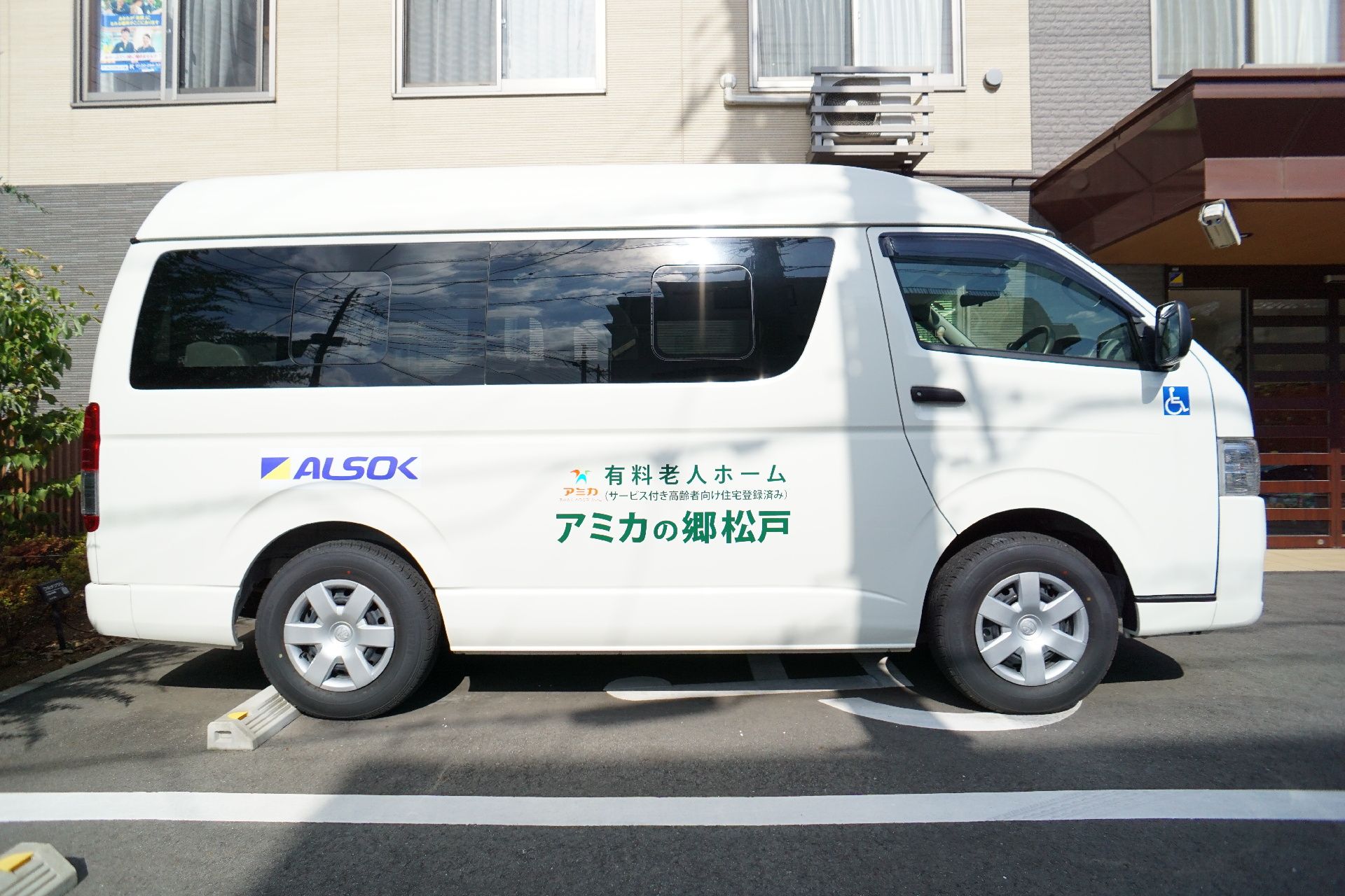 建物の手前にある駐車スペースに止まっている白いミニバン