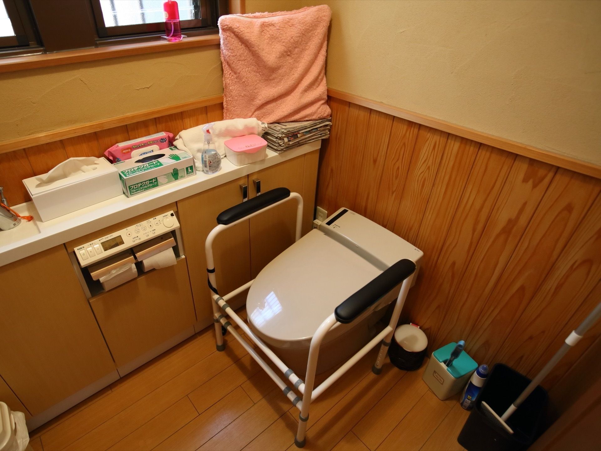 トイレの便座回りには手すりが設置されている。ウェットティッシュやゴム手袋など備品も手が届く位置に置かれている。
