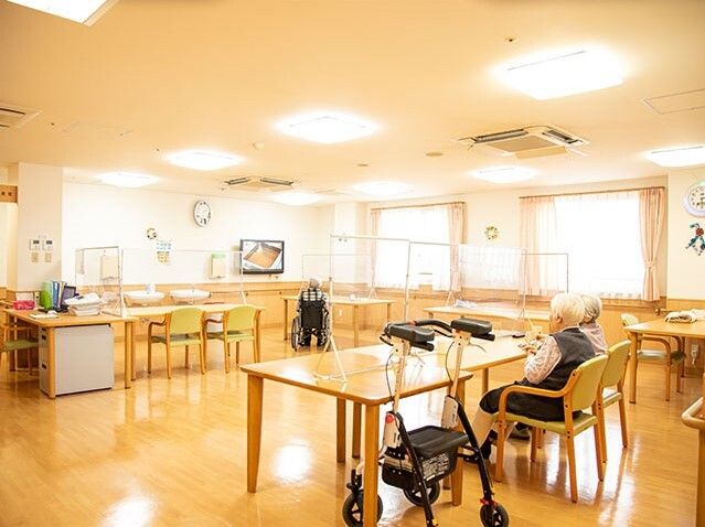 木製のダイニングテーブルが複数置かれた食堂の一つのテーブルでは、高齢女性2名が話している。
