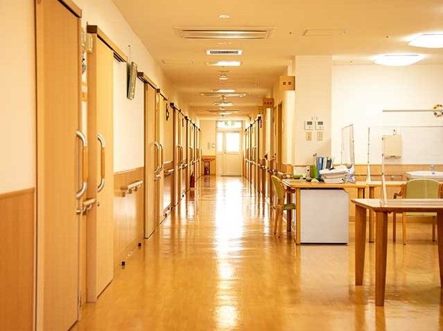 まっすぐな廊下の両サイドに手すりが設置され、居室のドアも並んでいる。突き当りには窓がある。